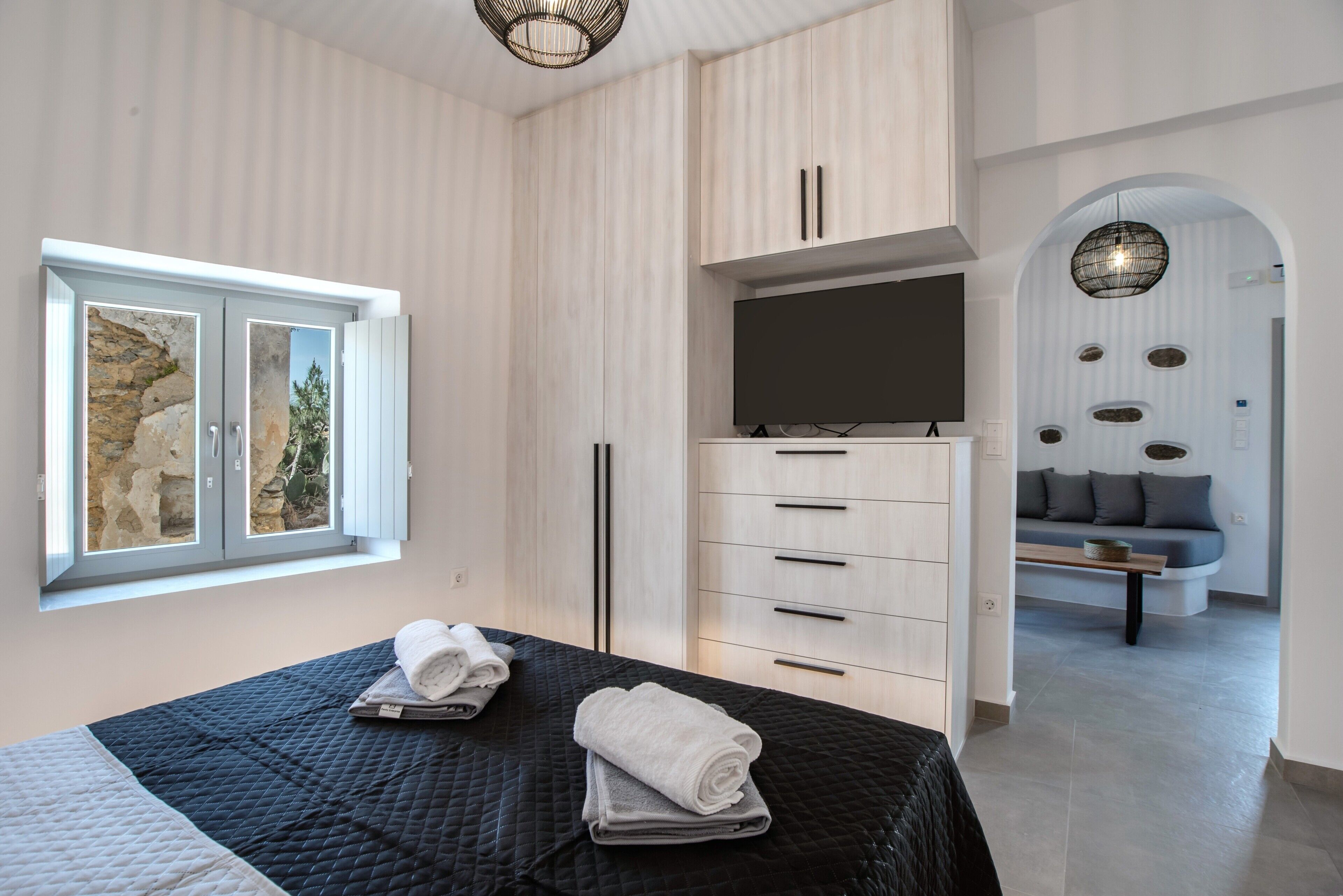 Une chambre moderne avec un lit, une armoire, un téléviseur et une vue sur un mur en pierre et de la verdure.