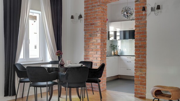 A dining area with a round table, black chairs, and a view into a kitchen with white cabinets and a brick column. - Parkowa 19 - Beach & Chill Sopot (Sopot)