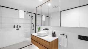 Ein modernes Badezimmer mit Duschkabine aus Glas, einem Holzbadezimmer-Möbelstück, einem großen Spiegel und einem weißen Waschbecken.