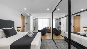 Ein modernes Hotelzimmer mit einem großen Bett, einer Sitzecke und einem dreiflügeligen Spiegelkleiderschrank.