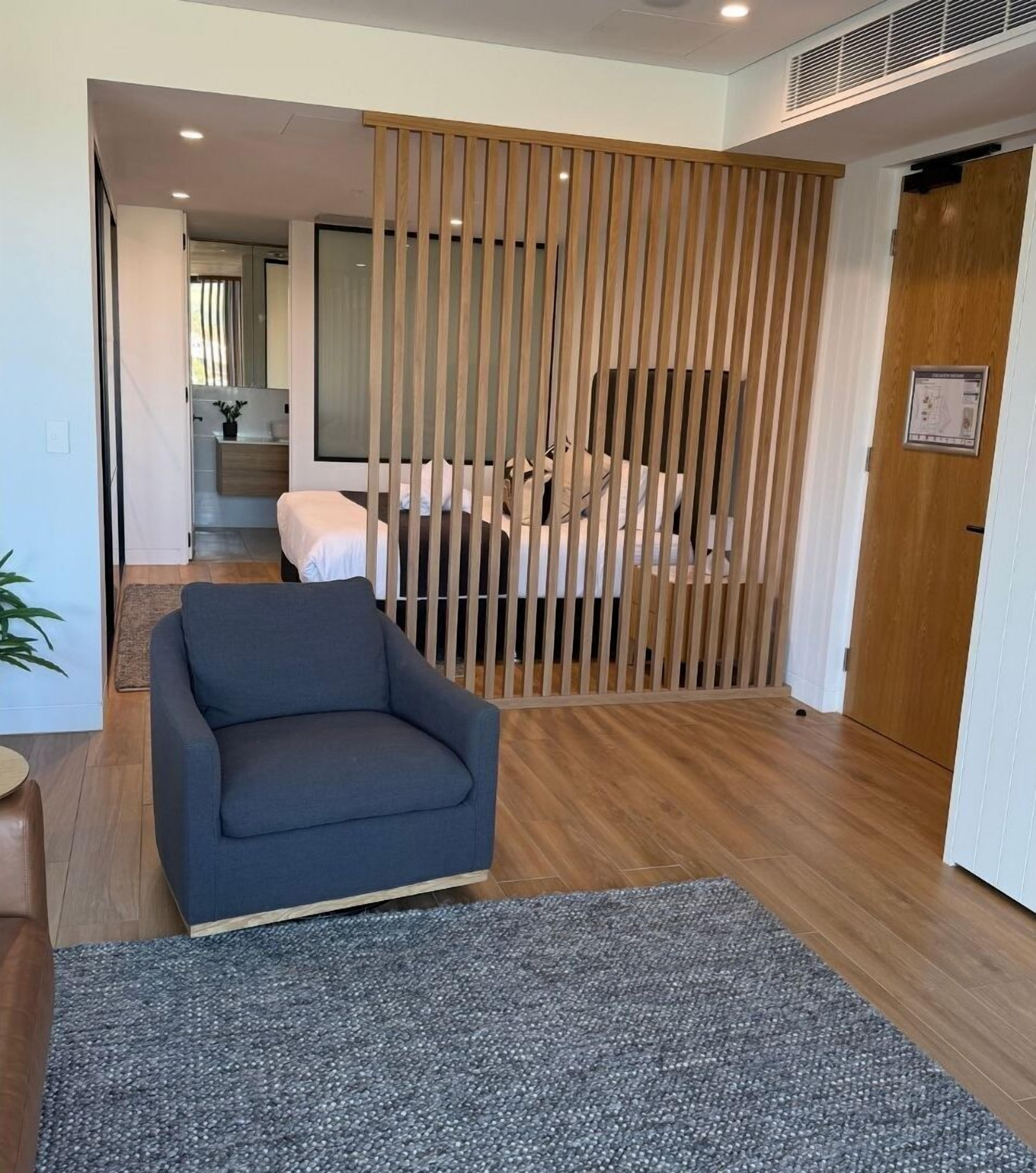 Una sala moderna con un sofá, un separador de madera y vistas a la cocina.