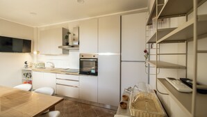 Una cocina moderna con armarios blancos, horno empotrado y zona de comedor con mesa y sillas de madera.