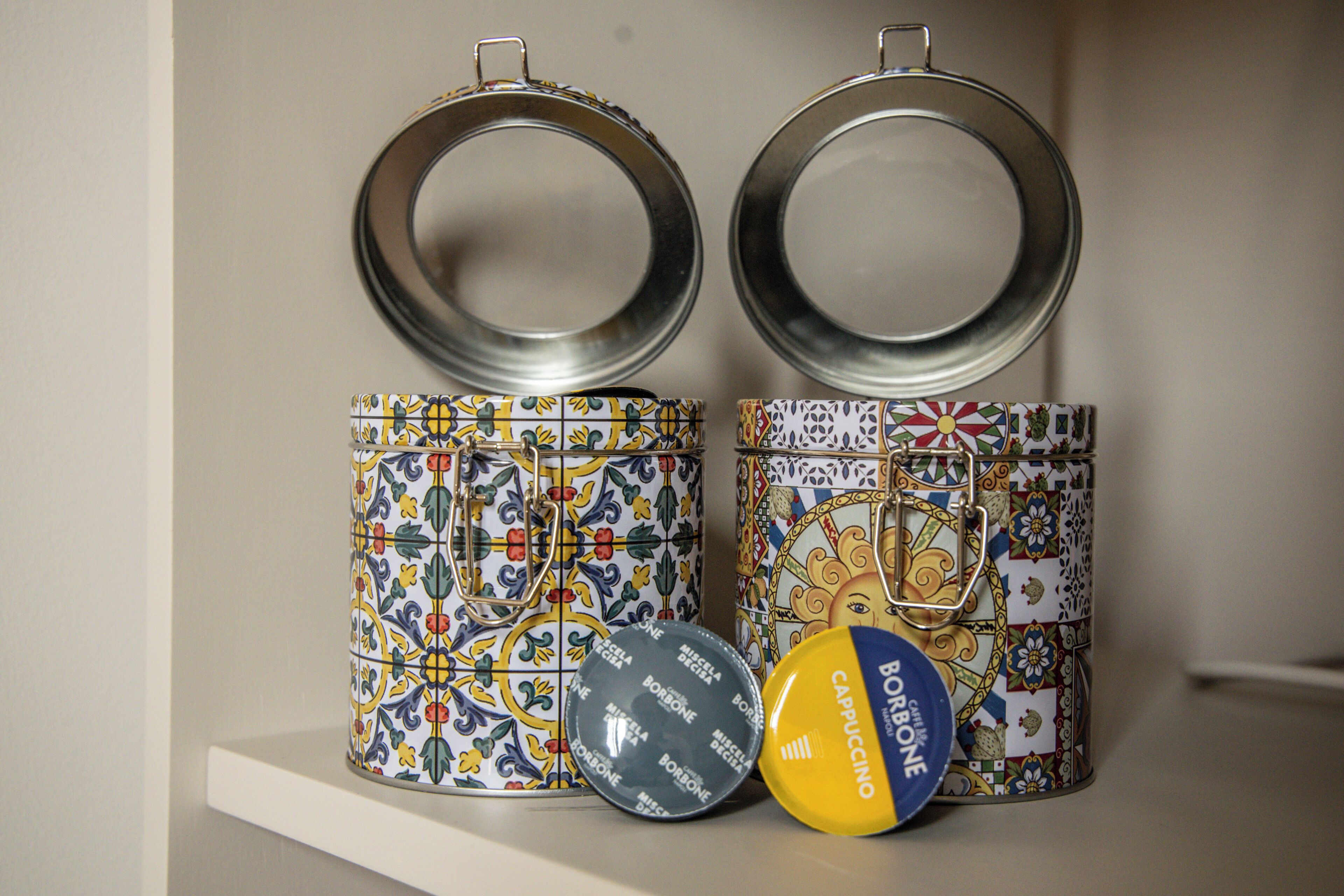 Two decorative metal containers with lids, a small blue and yellow container, and a patterned ceramic container.