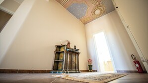 Una habitación con techo alto, decoración en el techo, chimenea, alfombra y una puerta.