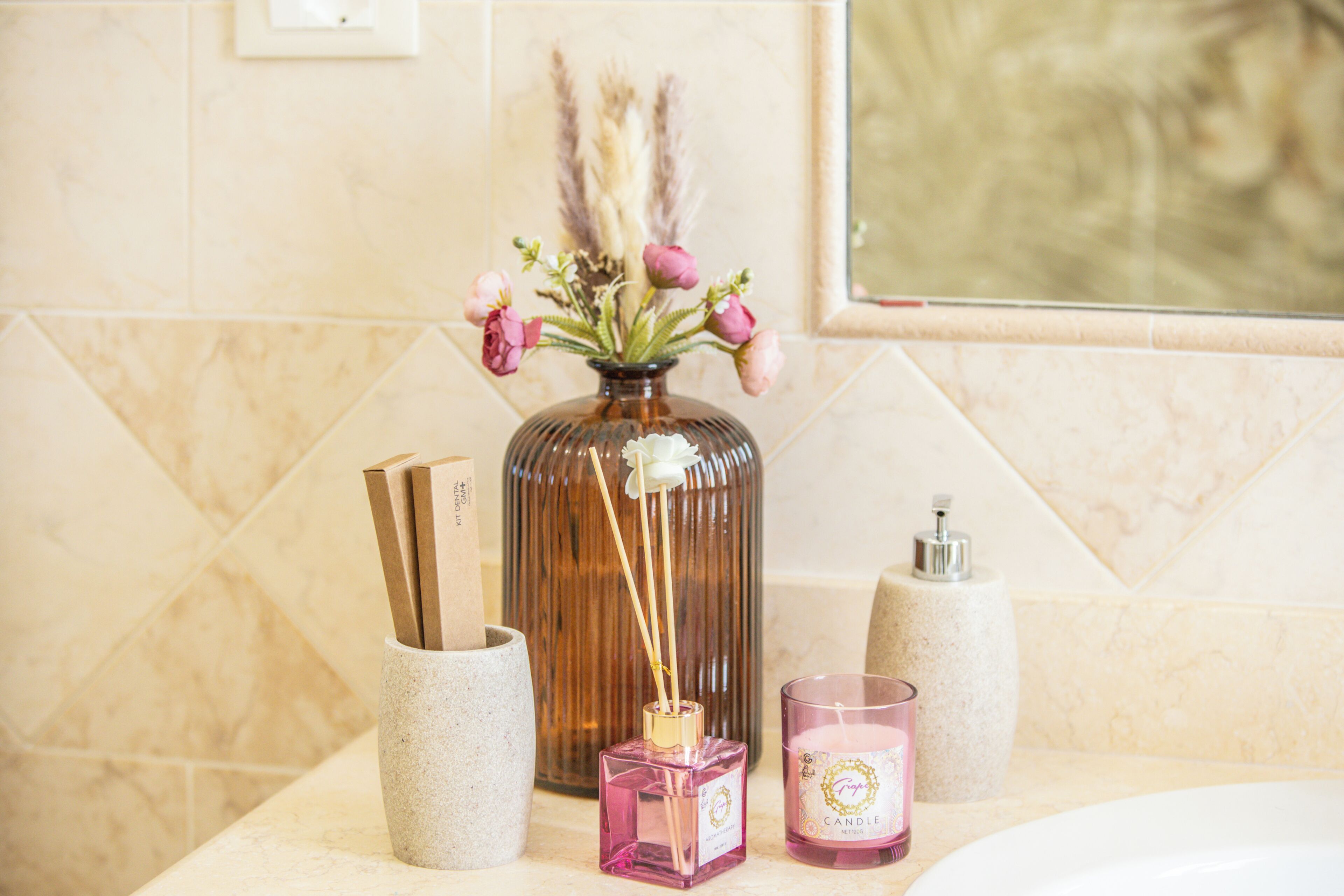 A bathroom vanity with a vase of flowers, a candle, and a diffuser.