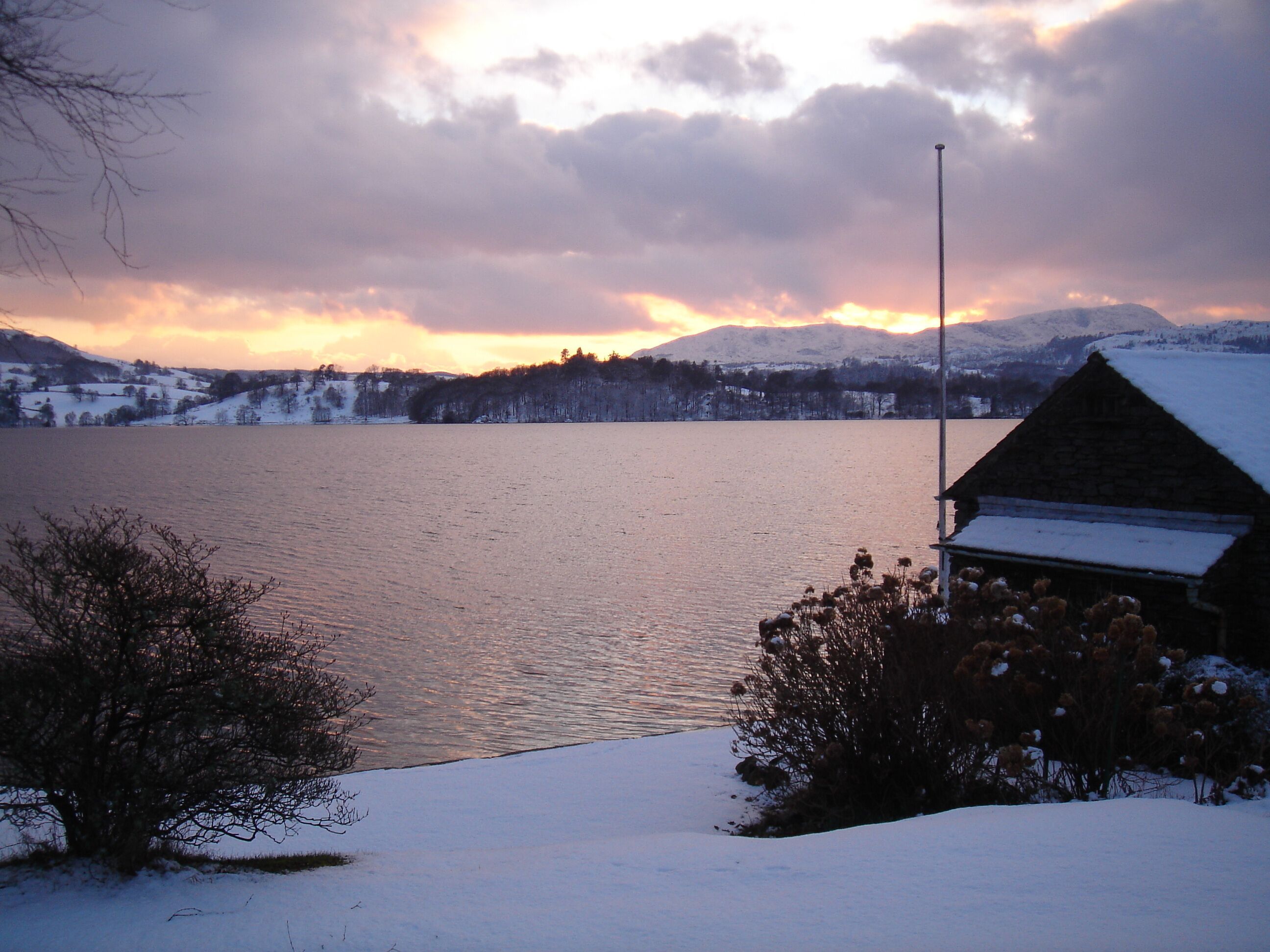 A snow-covered landscape with a lake, a mountain in the background, and a building with a snow-covered roof.