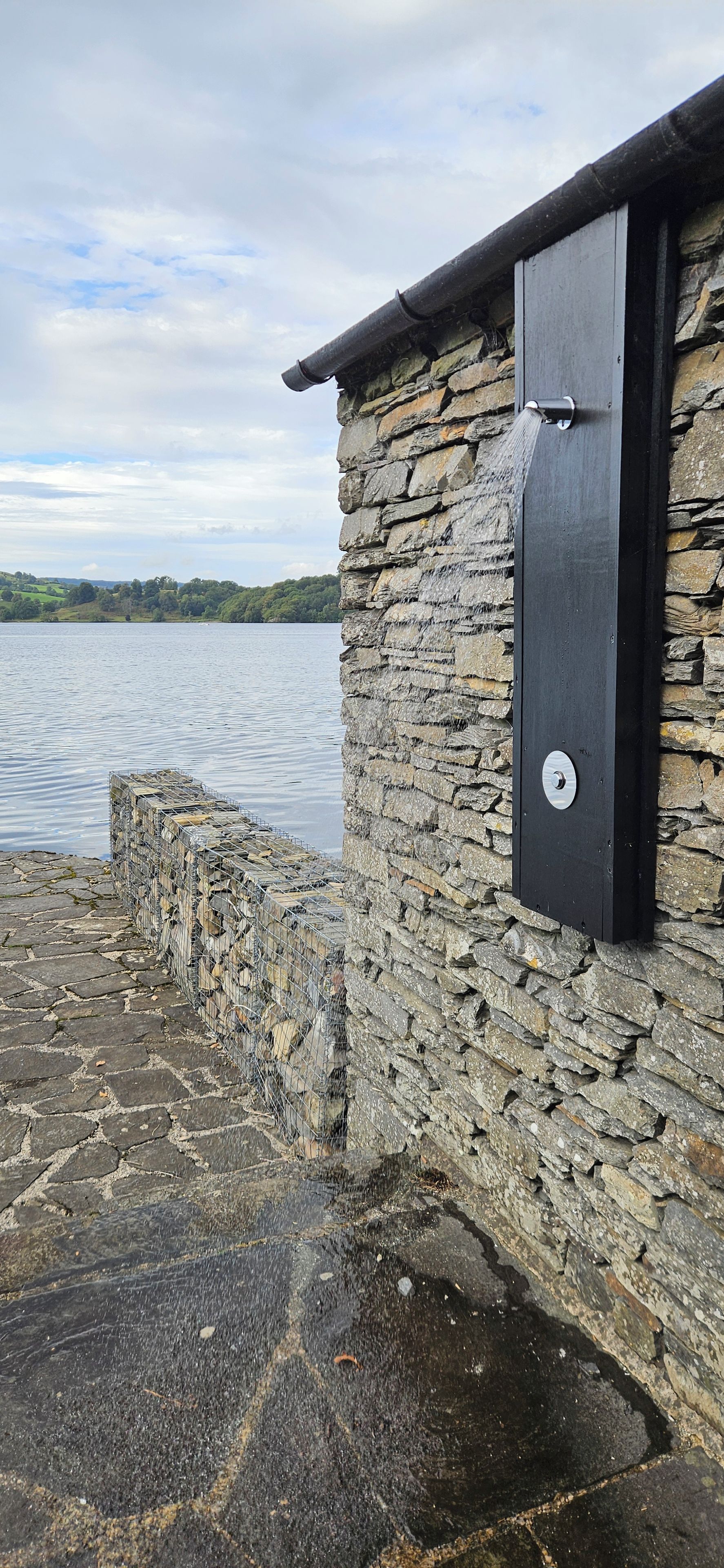 Edifício de pedra com porta de metal e vista para um lago.
