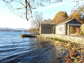 A stone building with a dock extending into a lake, surrounded by trees and mountains in the background. - Romantic Boathouse on Lake Windermere (Windermere)