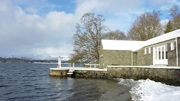 A stone building with a snow-covered roof, a dock extending into a lake, and snow on the ground.