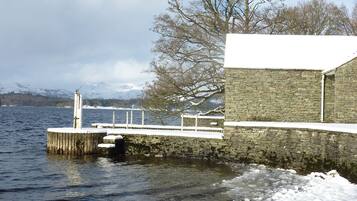 Un muelle de piedra se adentra en un lago, con nieve en el suelo y un edificio de piedra al fondo.