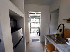 A compact kitchen with a refrigerator, a sink, and a small dining area with a table and chairs. - Cozy forest home one block from renowned Playa Grande surfing beach (Playa Grande)