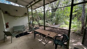 An enclosed outdoor area with a table and chairs, surrounded by a wire fence, overlooking a forested area. - Cozy forest home one block from renowned Playa Grande surfing beach (Playa Grande)