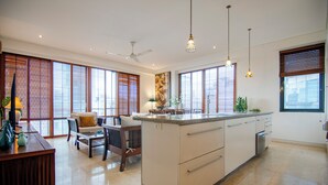 Une cuisine spacieuse dotée d’un îlot central, de grandes fenêtres équipées de stores, d’un ventilateur de plafond et de luminaires suspendus.