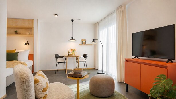 A modern living room with a sofa, ottoman, coffee table, TV, and a dining area with chairs and a table. - homie stay an der alten dampf (Würzburg)