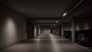 A dimly lit parking garage with concrete walls and a concrete floor, featuring several parked cars. - homie stay an der alten dampf (Würzburg)