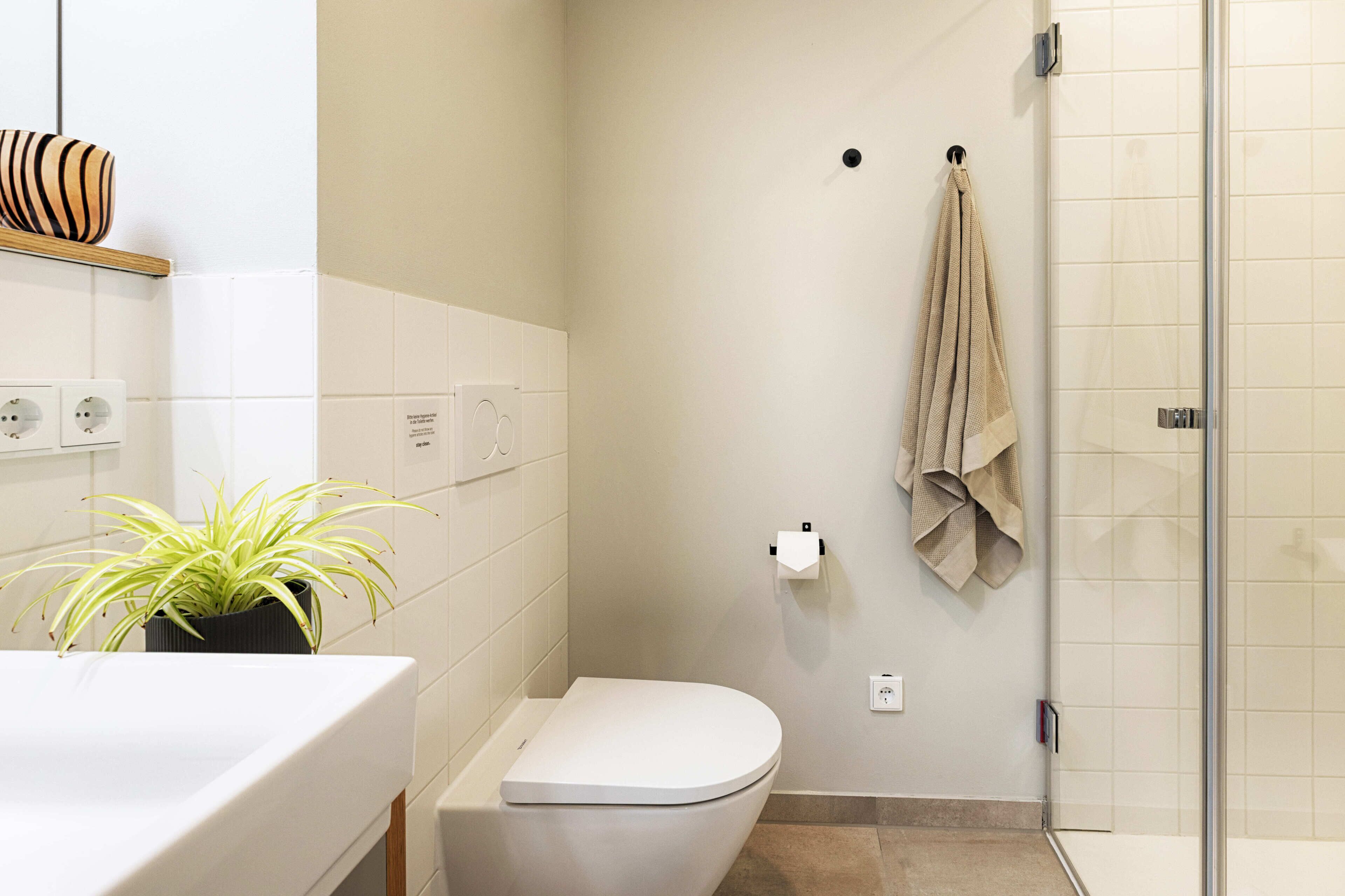 A bathroom with a toilet, a sink, a potted plant, a towel rack, and a shower area.