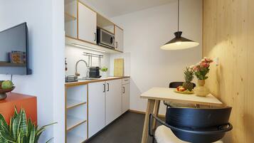 A compact kitchen with a microwave, toaster, and wooden cabinets. There's a dining table with a chair and a hanging light fixture.
