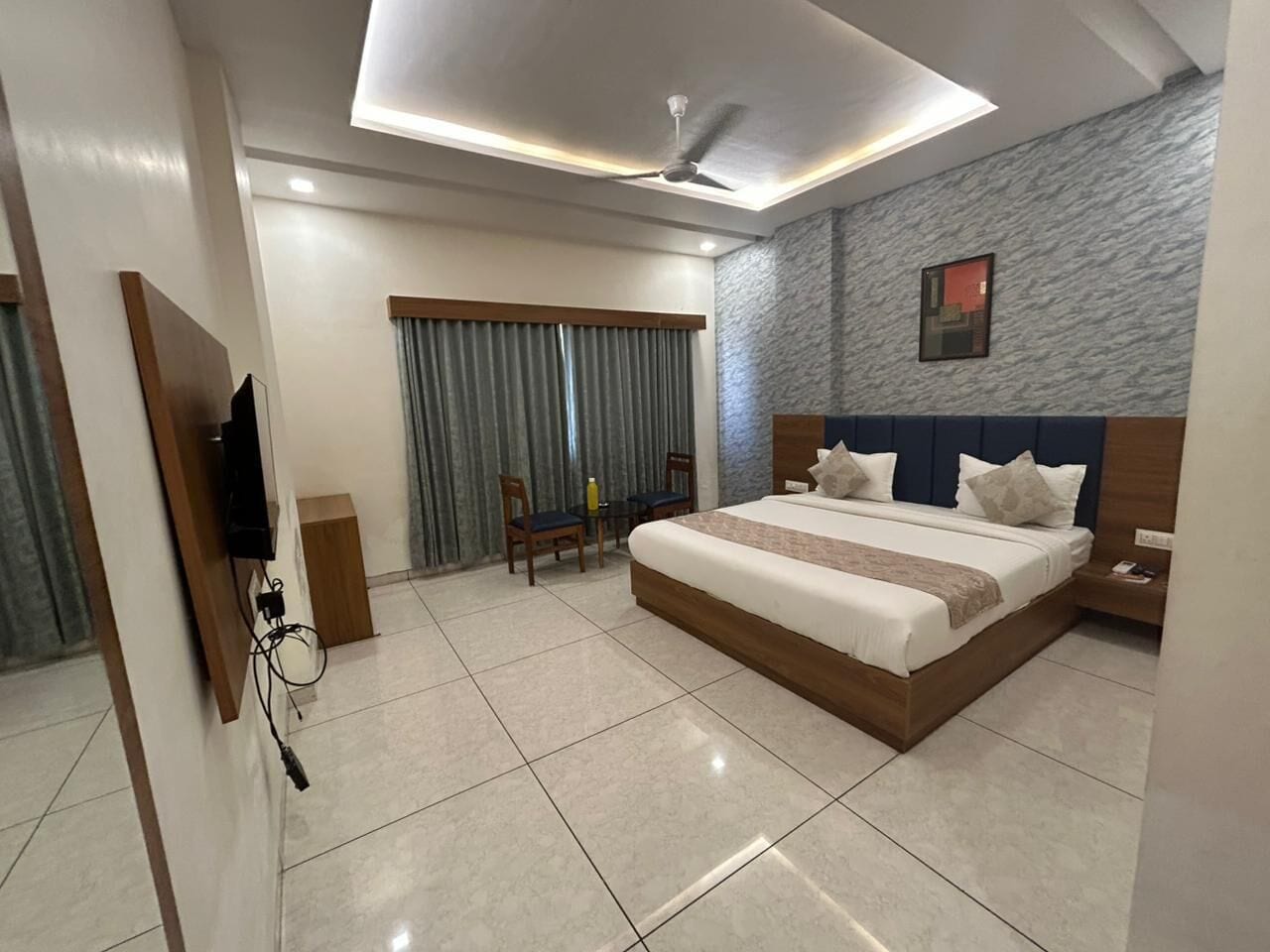 A hotel room with a bed, a desk, a chair, a TV, and a ceiling fan.