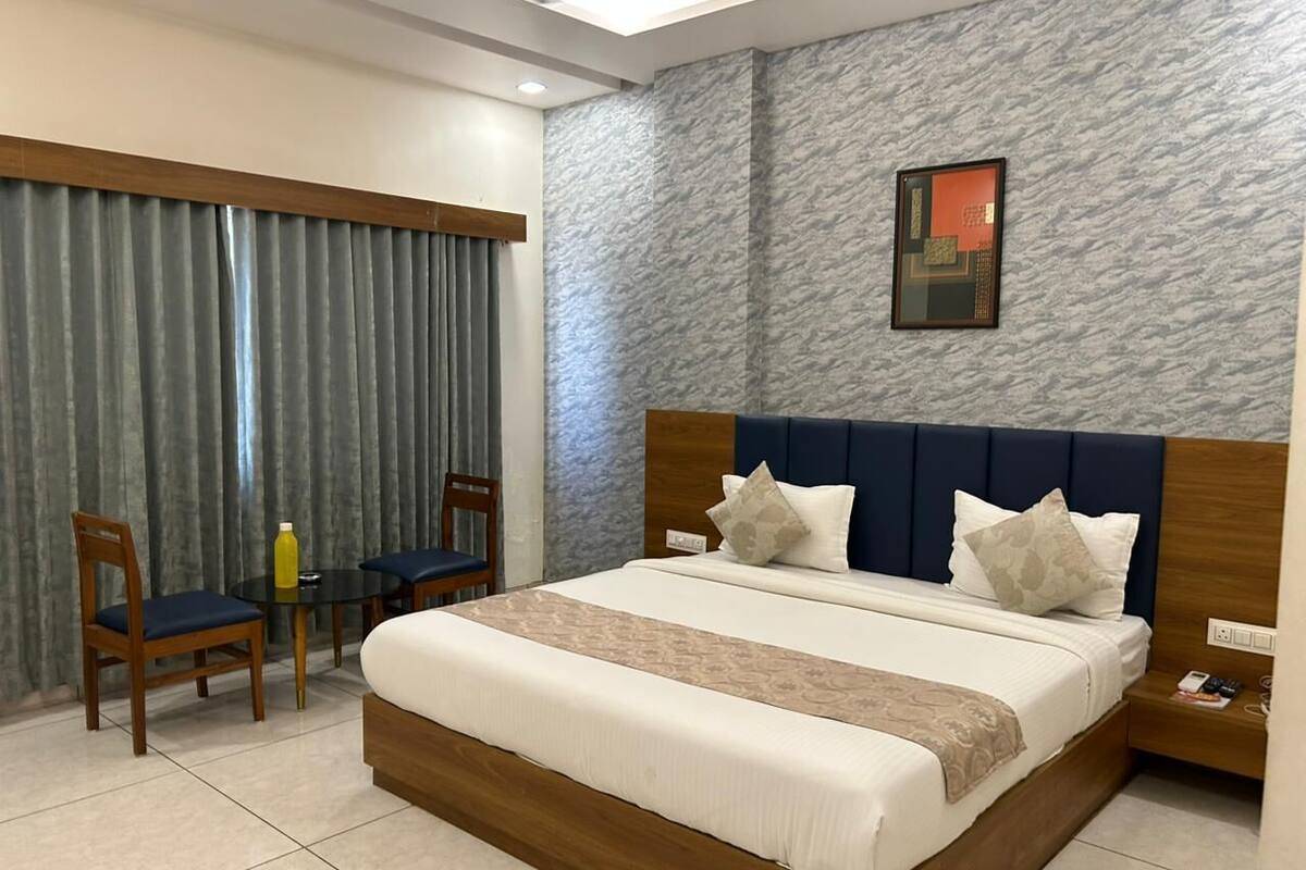 A hotel room with a bed, two chairs, a small table, a nightstand, and a window with curtains.