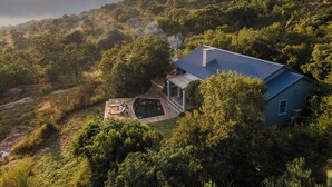 A house with a blue roof surrounded by dense greenery and hills.