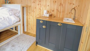 Une chambre avec un lit, un mur en bois, une petite kitchenette équipée d’un évier et une fenêtre.