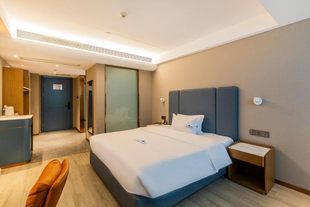 A hotel room with a bed, bedside table, and a desk with a chair.
