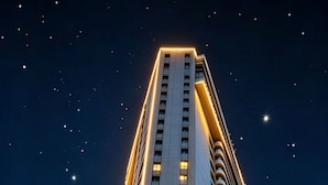Un moderno edificio de hotel con una entrada angular destacada, un paso de peatones en la parte delantera y un cielo nocturno despejado.