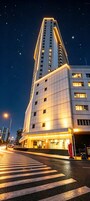 A modern hotel building with a prominent corner entrance, a crosswalk in front, and a clear night sky.