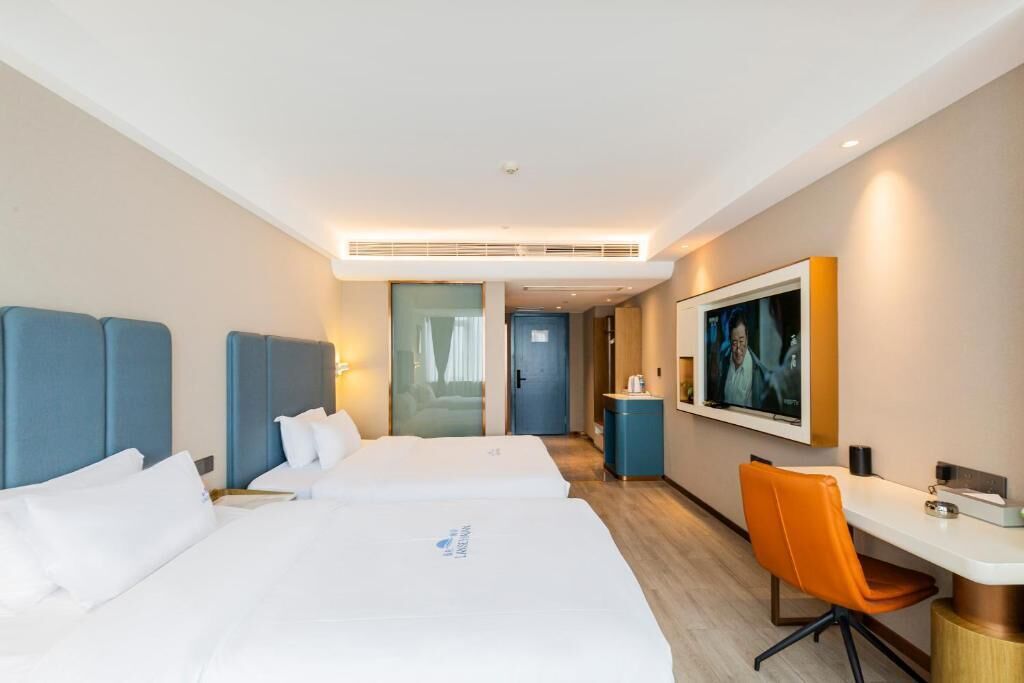 A hotel room with two beds, a desk, a chair, a TV, and a door leading to another room.