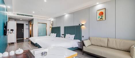 A hotel room with a large bed, a sofa, a dining table, and a small kitchen area.