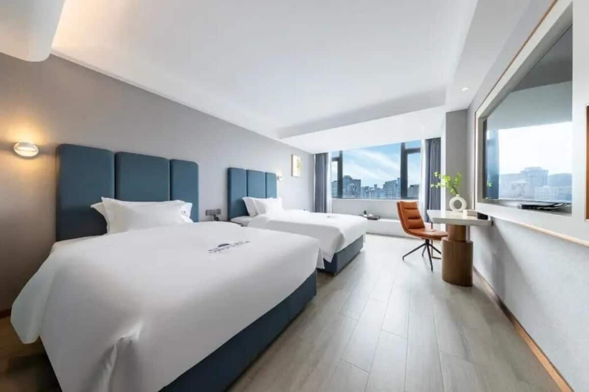 Una habitación de hotel moderna con dos camas, un escritorio y un amplio ventanal con vistas a la ciudad.