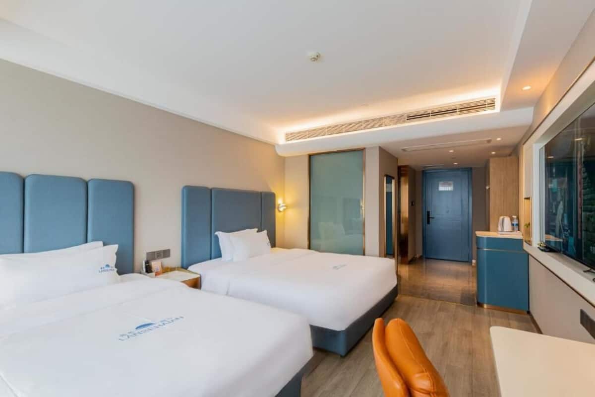 Habitación de hotel con dos camas, una kitchenette pequeña, un rincón de descanso y vistas a la ciudad.