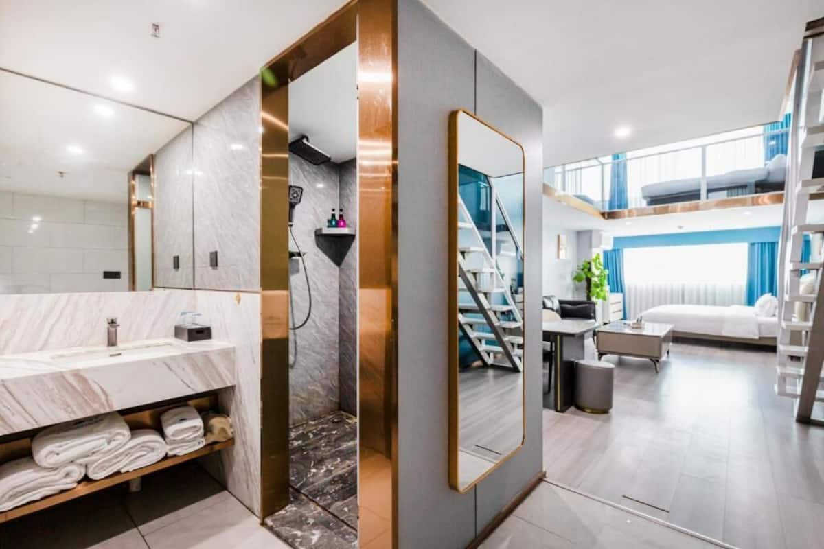 Una habitación de hotel moderna con baño de mármol, un espejo grande, una escalera y un balcón.