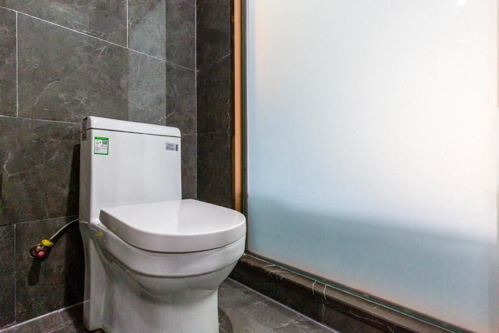 A toilet in a bathroom with dark marble walls and a glass shower enclosure.