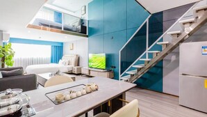 Una habitación de hotel moderna con zona de comedor, cama, televisor y escalera.