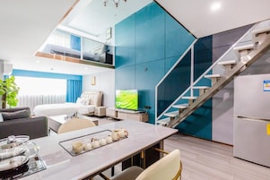A modern hotel room with a dining area, a bed, a TV, and a staircase.