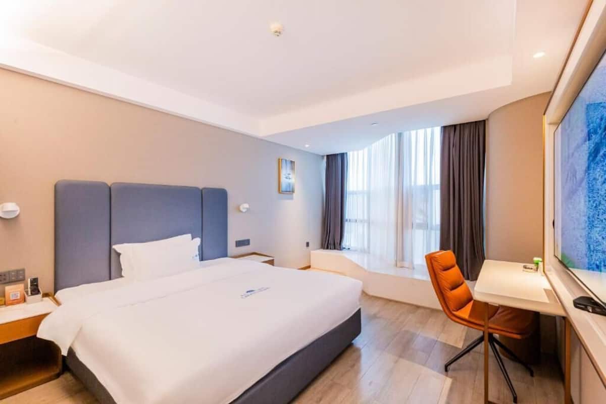 Una habitación de hotel con cama, escritorio, silla y un amplio ventanal.