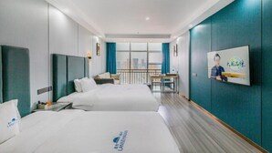 Habitación de hotel con dos camas, un escritorio, una silla, una ventana con vistas a la ciudad y un cuadro colgado en la pared.