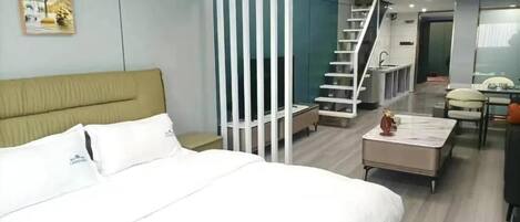 A hotel room with a bed, a desk, a chair, a staircase, and a view of the outdoor area.