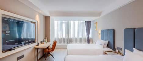A hotel room with two beds, a desk, a chair, a TV, and a window with curtains.