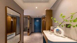 Un pasillo moderno de hotel con un espejo, una puerta azul, un tocador con artículos de aseo y una planta.