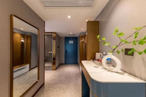 Un pasillo moderno de hotel con un espejo, una puerta azul, un tocador con artículos de aseo y una planta.