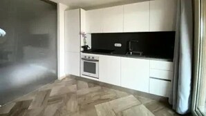 A modern kitchen with white cabinets, a black countertop, and a built-in oven. - PRESTIGE SHERDEN (Golfo Aranci)