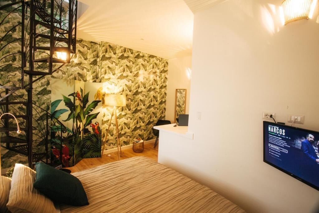 A room with a bed, a desk, a chair, a TV, a plant, and a staircase.