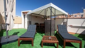 Una terraza en la azotea con dos sillones, una mesita, un área de estar cubierta y una pérgola.