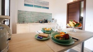 Una cocina con salpicadero de azulejos, una mesa de comedor con platos de comida y un frutero.