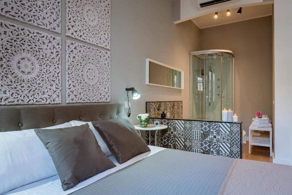 A bedroom with a bed, a bedside table with a lamp, a mirror, and a shower area.