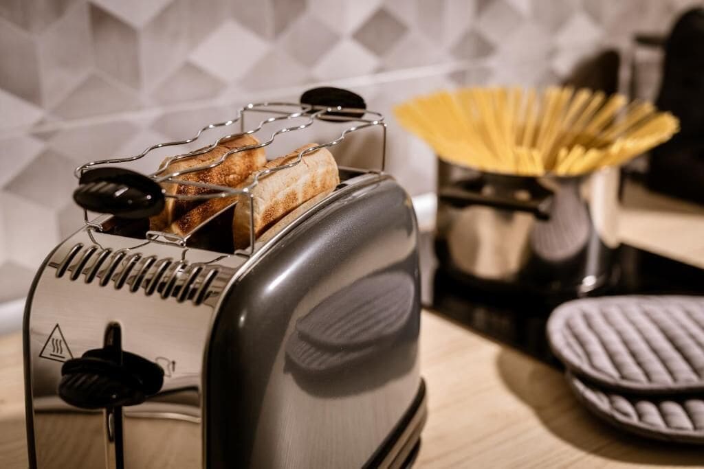 Un grille-pain avec des tranches de pain à l’intérieur, un panier rempli d’ustensiles et une gaufrière posée sur le plan de travail de la cuisine.