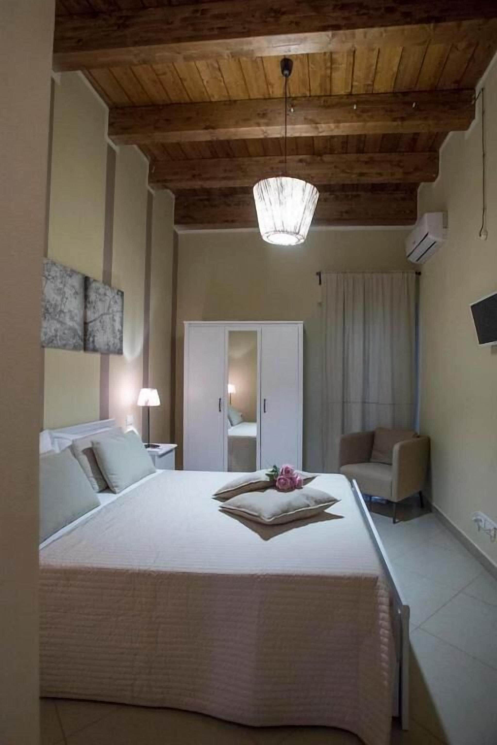 Um quarto com cama, mesa de cabeceira, guarda-roupa, cadeira e luminária no teto.
