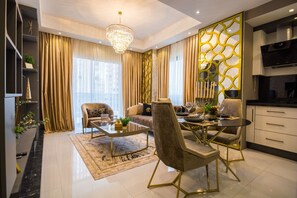 A modern living room with a dining area, a chandelier, and a kitchen with a TV. - Gold Sand Suites (Alanya)